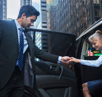 chauffeur helping female business person out of luxury vehicle