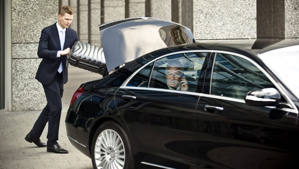 chauffeur putting luggage in back of luxury vehicle